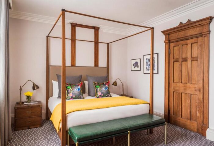 Kimpton Clocktower Hotel room. Four-poster bed with colorful pillows, yellow blanket, and green bench. Gay-friendly hotel room interior.
