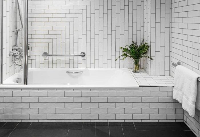 Kimpton Clocktower Hotel bathroom. White tiled walls, black floor, and a bathtub with glass screen. Gay-friendly hotel design. Modern, clean style.