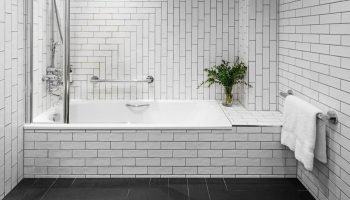 Kimpton Clocktower Hotel bathroom. White tiled walls, black floor, and a bathtub with glass screen. Gay-friendly hotel design. Modern, clean style.