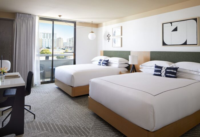 Gay-Friendly Kimpton Hotel Enso room with two beds, desk, balcony, and city view. Modern decor, white linens, and stylish design. Gay travel lodging.