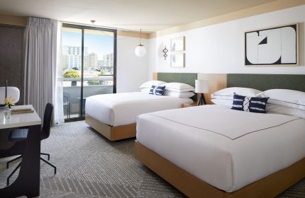 Gay-Friendly Kimpton Hotel Enso room with two beds, desk, balcony, and city view. Modern decor, white linens, and stylish design. Gay travel lodging.