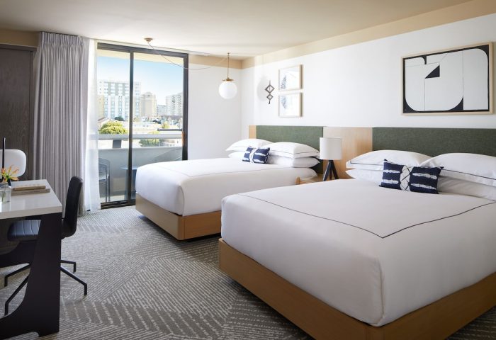 Gay-Friendly Kimpton Hotel Enso room with two beds, desk, balcony, and city view. Modern decor, white linens, and stylish design. Gay travel lodging.