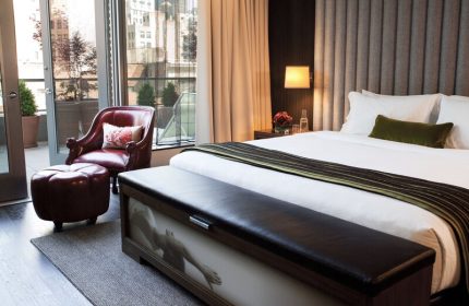 Kimpton Hotel Eventi's gay-friendly room. Balcony, city view, leather chair and ottoman, bed with bench. Modern design for gay men travelers.