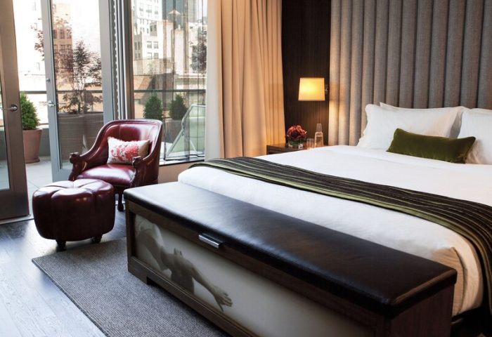 Kimpton Hotel Eventi's gay-friendly room. Balcony, city view, leather chair and ottoman, bed with bench. Modern design for gay men travelers.