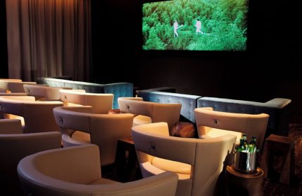 Kimpton Hotel Eventi gay-friendly cinema. Theater seating with curved chairs, couches, and a large screen showing men running in a forest.