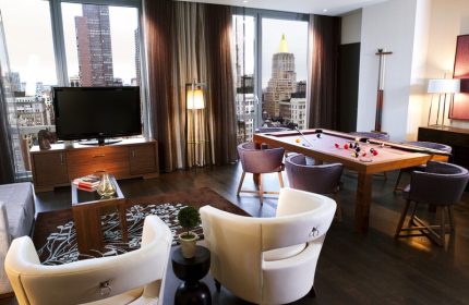 Kimpton Hotel Eventi's gay-friendly suite with a pool table, chairs, and a TV, offering a luxurious stay in NYC. Great for gay travelers.