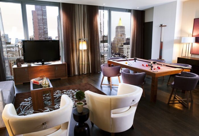 Kimpton Hotel Eventi's gay-friendly suite with a pool table, chairs, and a TV, offering a luxurious stay in NYC. Great for gay travelers.
