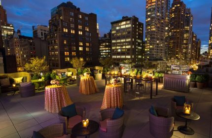 Kimpton Hotel Eventi rooftop lounge at night. Gay-friendly hotel with city views, tables, chairs, and bar. Ideal for events and gay travel.