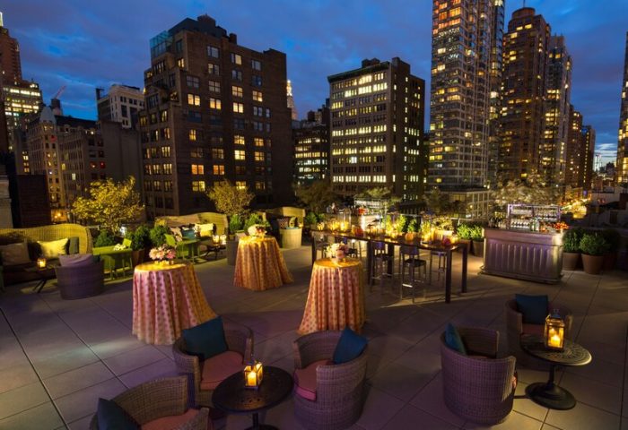 Kimpton Hotel Eventi rooftop lounge at night. Gay-friendly hotel with city views, tables, chairs, and bar. Ideal for events and gay travel.