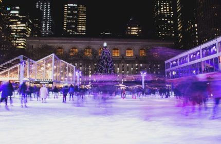 Kimpton Hotel Eventi: Ice skaters at Bryant Park rink, near gay-friendly hotel. Christmas tree and NYC buildings in background. Night scene.