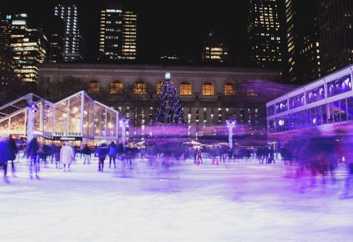 Kimpton Hotel Eventi: Ice skaters at Bryant Park rink, near gay-friendly hotel. Christmas tree and NYC buildings in background. Night scene.