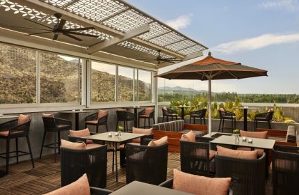 Outdoor dining at gay-friendly Kimpton Rowan Palm Springs Hotel. Rooftop bar with mountain views, tables, chairs, and umbrellas. Stylish hotel.