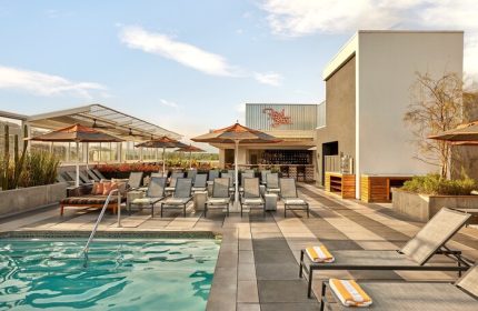 Rooftop pool and bar at Kimpton Rowan Palm Springs Hotel. Gay-friendly hotel with lounge chairs, umbrellas, and a stylish bar area. Palm Springs travel.