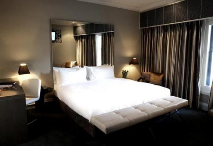 Kirketon Hotel Sydney room. Gay-friendly hotel bedroom with a large bed, white linens, a bench, and striped curtains. Modern design.