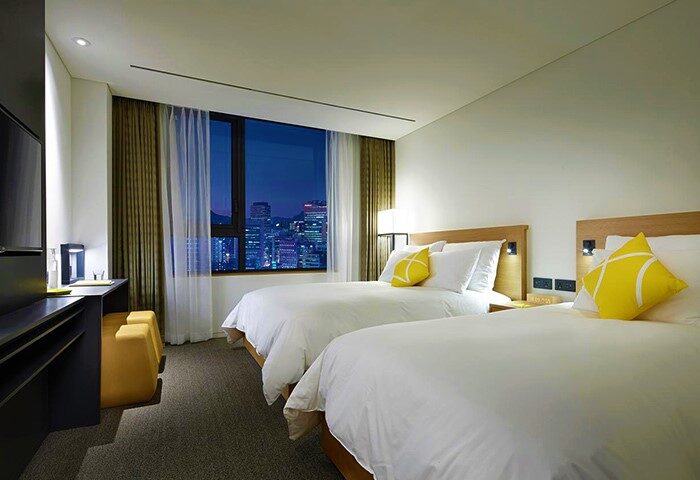 L7 Myeongdong by LOTTE hotel room with twin beds. Gay-friendly hotel with city view at night. Ideal for gay travel in Seoul, South Korea.