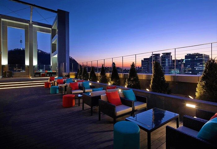 L7 Myeongdong by LOTTE rooftop terrace at dusk. Gay-friendly hotel with Seoul Tower view. Stylish seating, perfect for gay travel in Seoul.