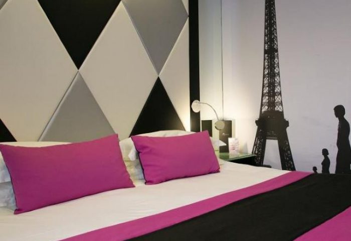 L'Empire Paris Hotel room with Eiffel Tower wall art. Gay-friendly, pet-friendly hotel interior with modern design and pink pillows.