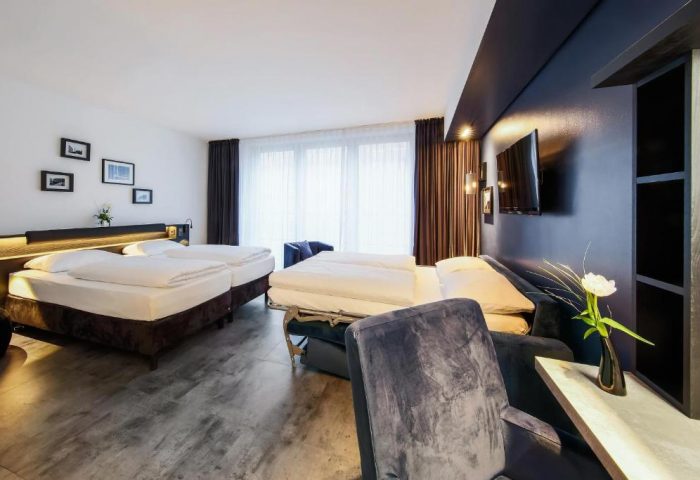 Lindemann's Hotel: Interior of a gay-friendly hotel room. Features twin beds, a sofa bed, dark blue accent wall, and modern decor.