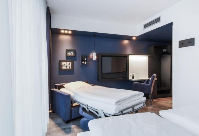 Lindemann's Hotel room. Gay-friendly hotel with a bed, desk, TV, and chair. Modern design with blue accents. Comfortable stay for gay travelers.