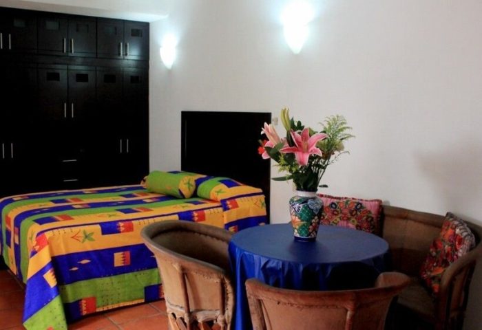 La Iguana Vallarta LGBT adults-only hotel room. Colorful bedspread, table with flowers, and dark wood wardrobe. Romantic Zone stay.