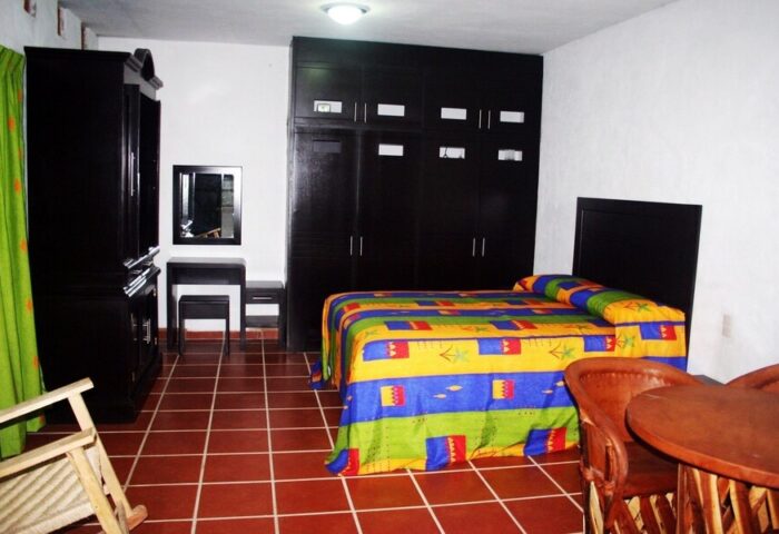 La Iguana Vallarta LGBT adults-only hotel room in Romantic Zone. Colorful bedspread, dark wood furniture, and tiled floor. Gay-friendly stay.