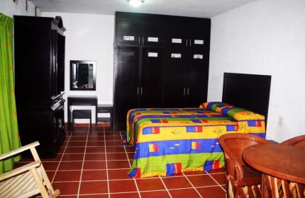 La Iguana Vallarta LGBT adults-only hotel room in Romantic Zone. Colorful bedspread, dark wood furniture, and tiled floor. Gay-friendly stay.