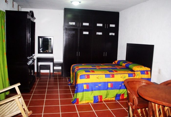 La Iguana Vallarta LGBT adults-only hotel room in Romantic Zone. Colorful bedspread, dark wood furniture, and tiled floor. Gay-friendly stay.