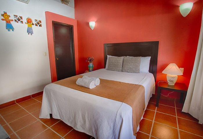 La Iguana Vallarta LGBT adults-only hotel room in Romantic Zone. Bed with towels, red wall, and playful decor. Gay-friendly lodging.