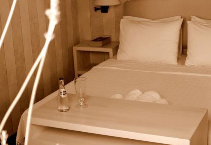 La Maison Kalogera, gay-friendly hotel room. Sepia toned bedroom with white linens, water bottle, glass, and bedside table. Cozy, inviting space.