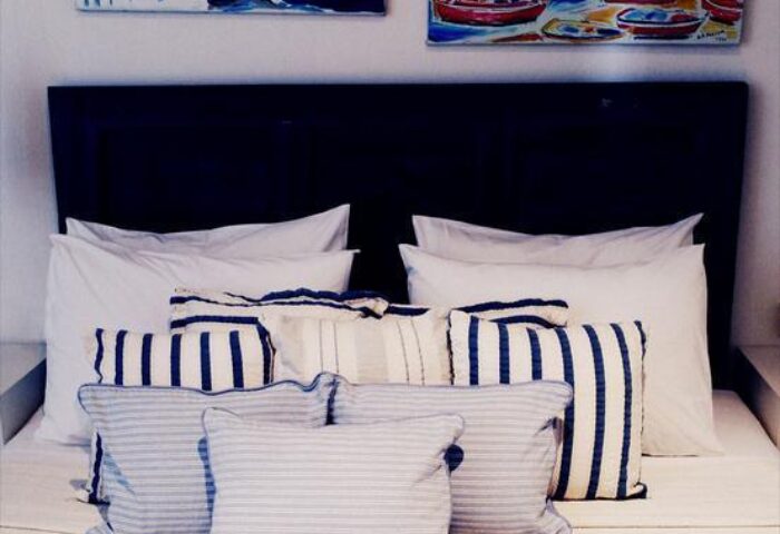 La Maison Kalogera, gay-friendly hotel: Bedroom with striped pillows, white linens, and paintings of Mykonos. Gay travel lodging.