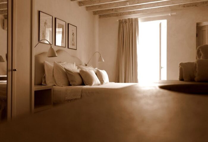La Maison Kalogera gay-friendly hotel room. Neutral tones, bed with pillows, wall art, and bright window. Ideal for gay men's travel in Mykonos.