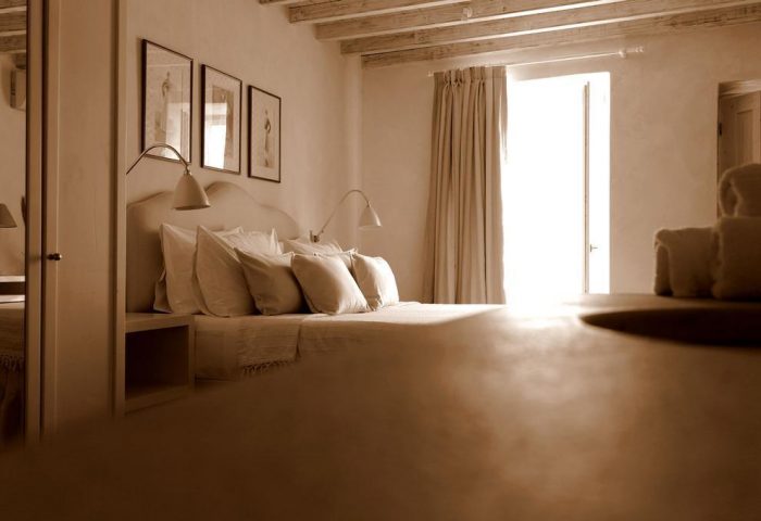 La Maison Kalogera gay-friendly hotel room. Neutral tones, bed with pillows, wall art, and bright window. Ideal for gay men's travel in Mykonos.