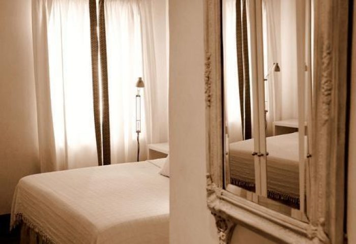 La Maison Kalogera gay-friendly hotel room. Sepia toned bedroom with a bed, window and a large ornate mirror. Gay travel advice.