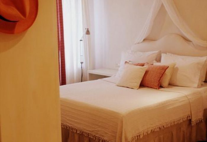 La Maison Kalogera gay-friendly hotel room. Cozy bed with canopy, wooden floors, and exposed beams. Ideal for gay men's travel in Mykonos.