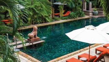 La Residence d'Angkor, A Belmond Hotel, Siem Reap pool. Gay-friendly hotel with lush greenery, lounge chairs, and a statue fountain.