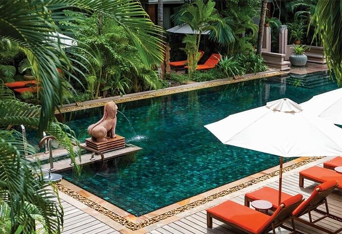 La Residence d'Angkor, A Belmond Hotel, Siem Reap pool. Gay-friendly hotel with lush greenery, lounge chairs, and a statue fountain.