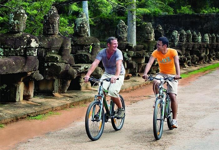 Gay men biking near La Residence d'Angkor, a Belmond Hotel, Siem Reap. Stone statues line the road. Gay-Friendly Hotel in Cambodia.