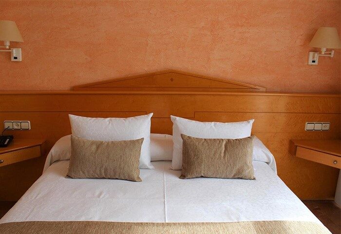 La Santa Maria gay-friendly hotel room. Double bed with pillows, side tables, and lamps. Orange textured wall. Gay travel advice.