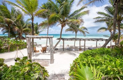La Valise Tulum: Gay-friendly hotel beach view. Palm trees, white sand, and ocean. A tropical paradise for gay men's travel.