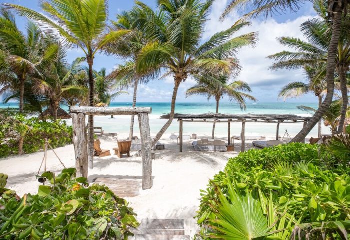 La Valise Tulum: Gay-friendly hotel beach view. Palm trees, white sand, and ocean. A tropical paradise for gay men's travel.