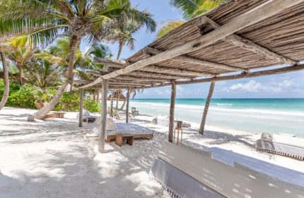La Valise Tulum gay-friendly hotel beach view. Thatched roof, palm trees, and ocean scene. Ideal for gay men's travel in Tulum, Mexico.