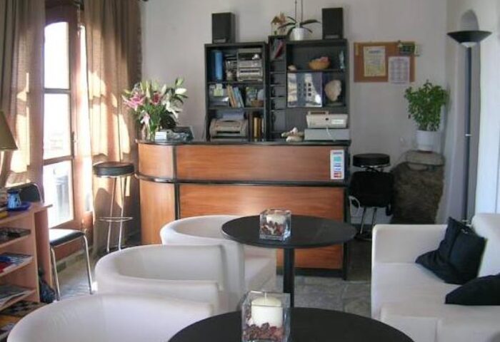 La Veranda of Mykonos Traditional Guesthouse's lobby. Gay-friendly hotel reception area with seating, desk, and bookshelf. Mykonos travel.