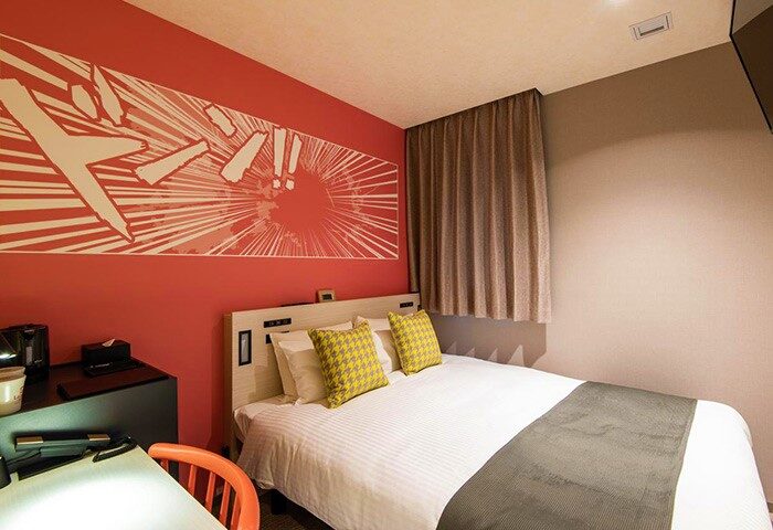 L'gent Hotel Shinjuku Kabukicho room. Gay-friendly hotel with double bed, yellow pillows, and manga art on the red wall. Modern, clean design.