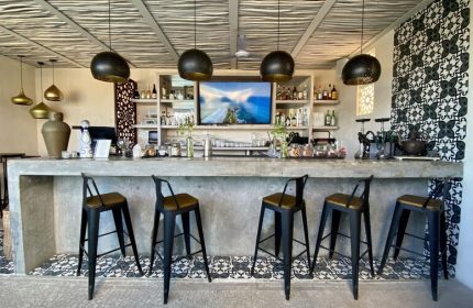 Layla Tulum Adults Only gay-friendly hotel bar. Interior view of bar with stools, shelves with bottles, patterned tiles, and pendant lights.