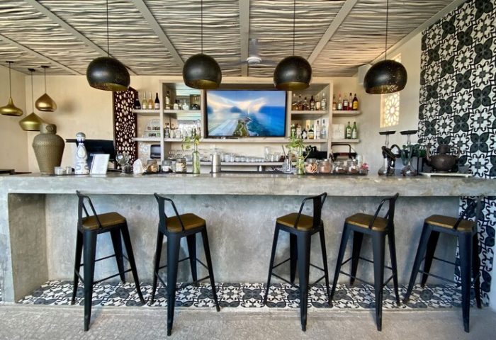 Layla Tulum Adults Only gay-friendly hotel bar. Interior view of bar with stools, shelves with bottles, patterned tiles, and pendant lights.