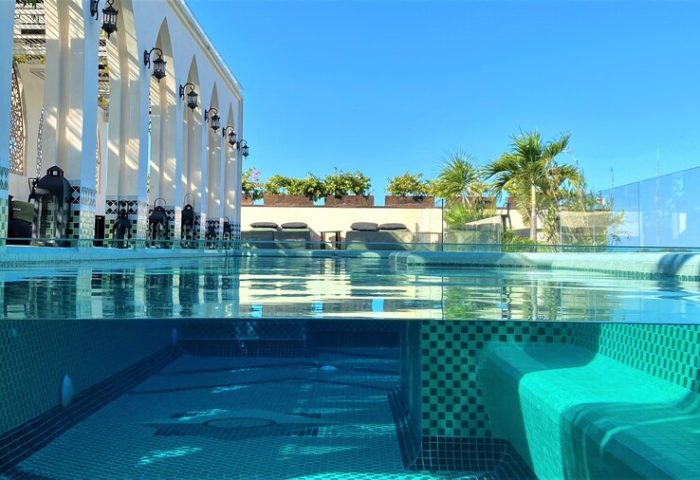 Layla Tulum Adults Only gay-friendly hotel pool. Underwater view of the pool, with lounge chairs and palm trees in the background.