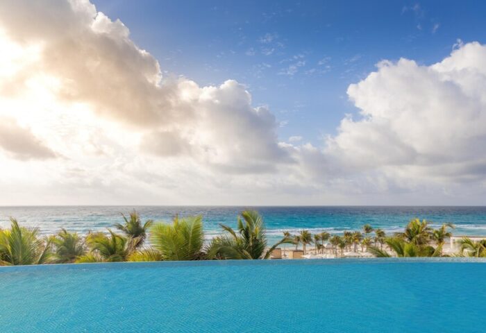 Infinity pool view at Le Blanc Resort Cancun Adults Only. All-inclusive, gay-friendly hotel with ocean backdrop and palm trees.