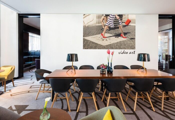 Le Méridien Munich hotel's stylish lounge area. A long table with chairs, lamps, and art. Gay-friendly hotel design in Munich, Germany.