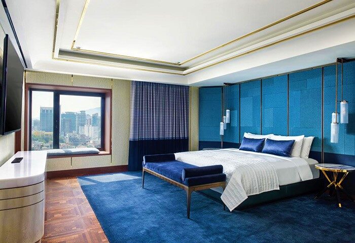 Le Meridien Seoul gay-friendly hotel room. Blue decor, city view, bed, and bench. Modern design for LGBT travelers in Seoul.