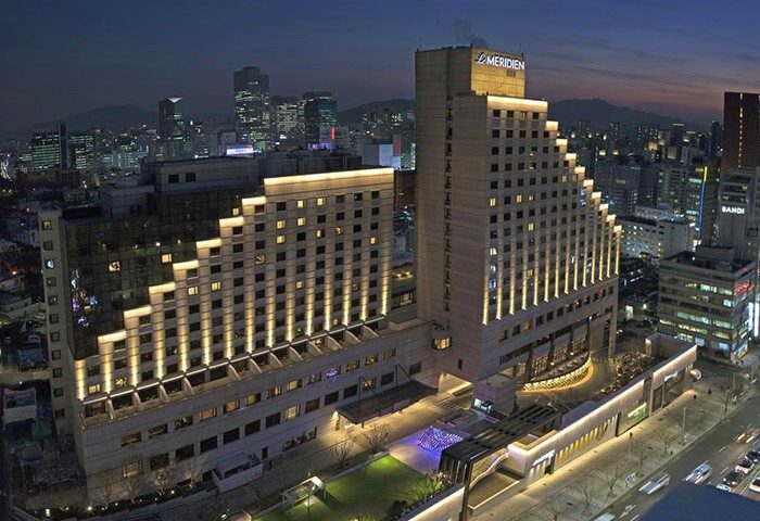 Le Meridien Seoul, a gay-friendly hotel, at night. The building is lit up with lights, and the city skyline is in the background.